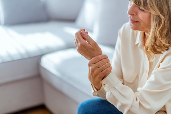 Photo of Painful Wrist In An Elderly Person. Senior woman suffering from pain in wrist at home while sitting on a gray sofa. Mature woman feeling wrist pain, injury problem, healthcare concept, sprain